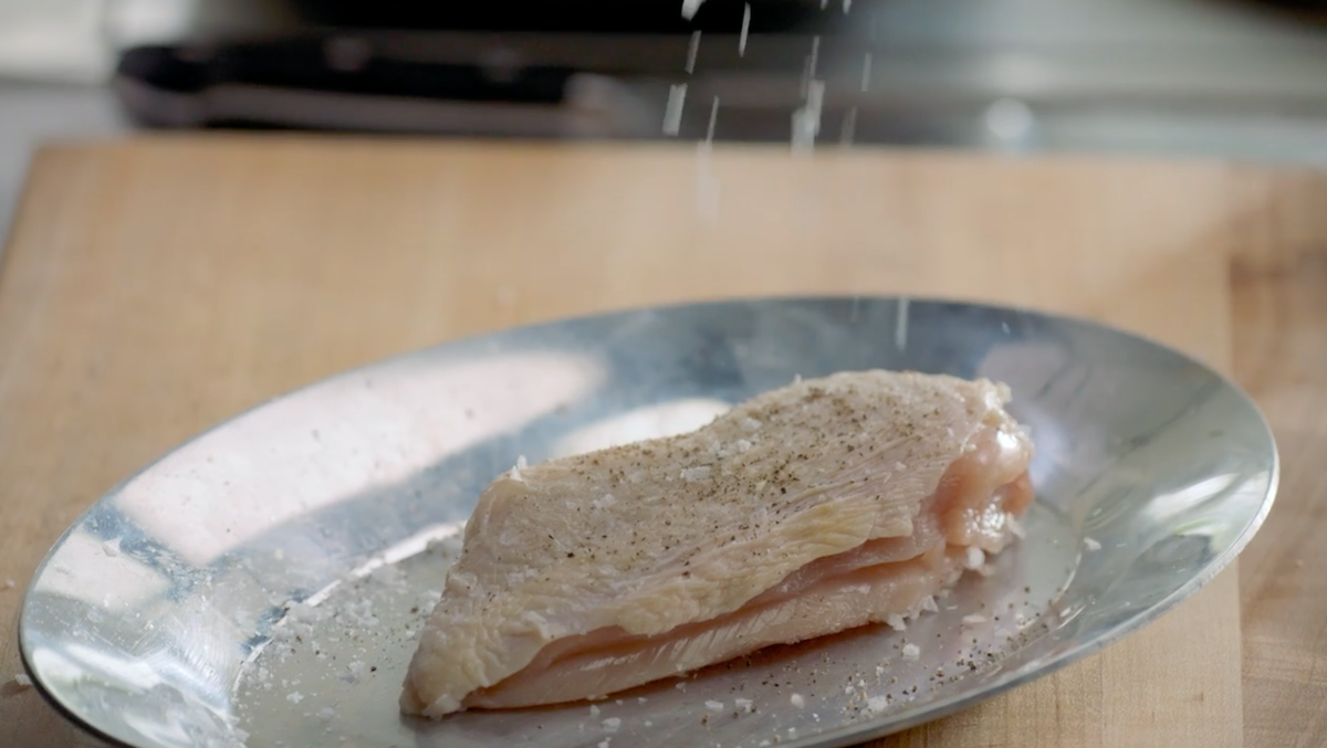 Raw chicken being seasoned on silver plate