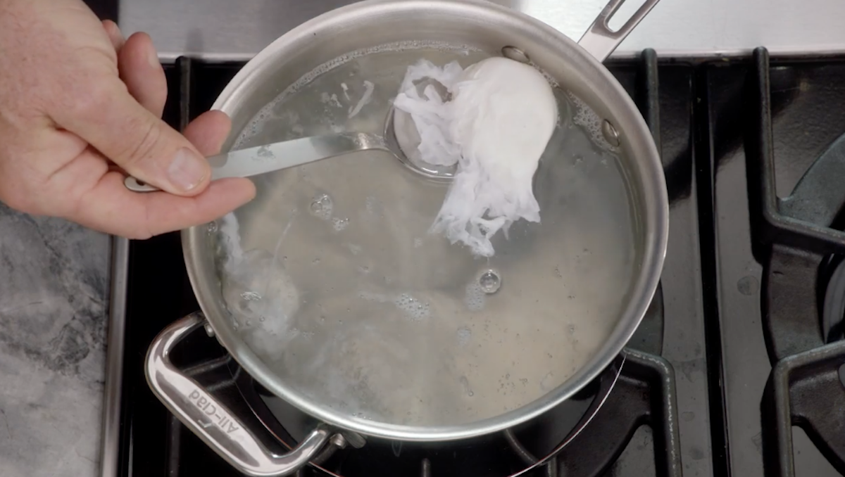 Poached egg being lifted out of water with spoon