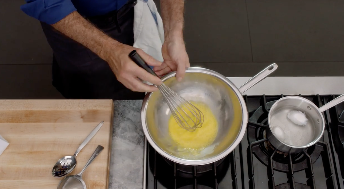 Thomas Keller whisking eggs in bowl over pot