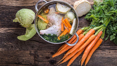 Chicken and carrots in pot with raw cabbage and carrots on wood table