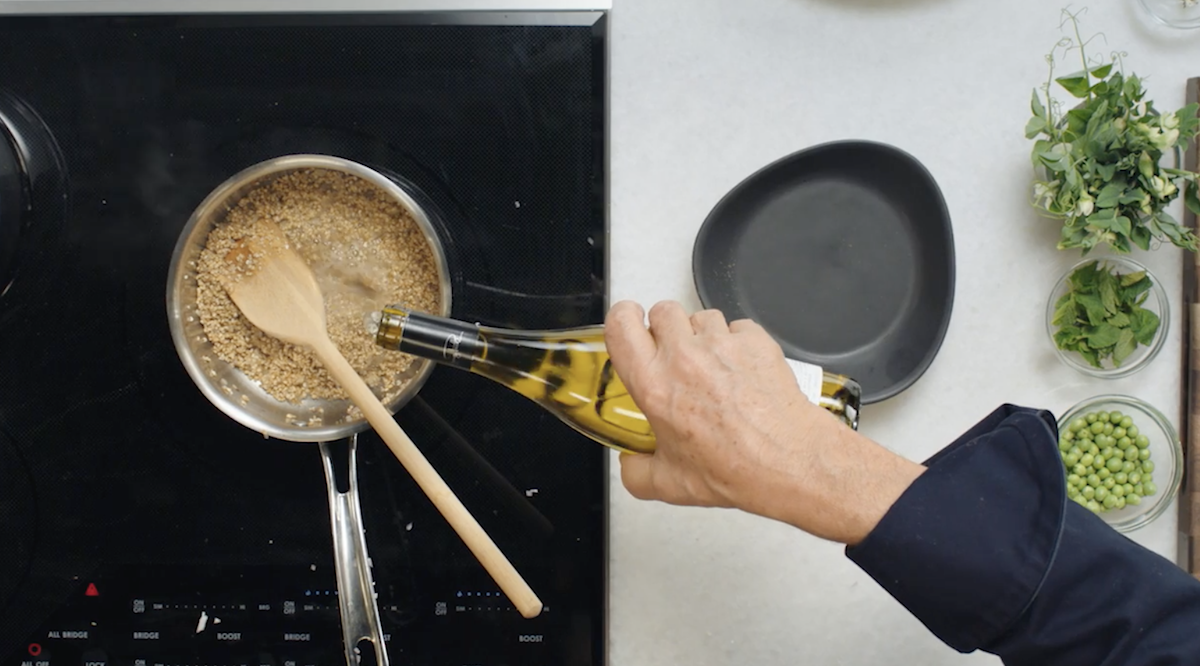 Wolfgang Puck pouring white wine into oats on stove