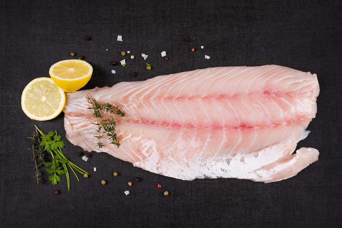 Raw perch filet with lemon and seasoning on black background