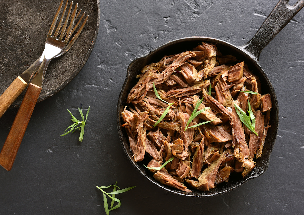 Braised meat in cast iron skillet with utensils