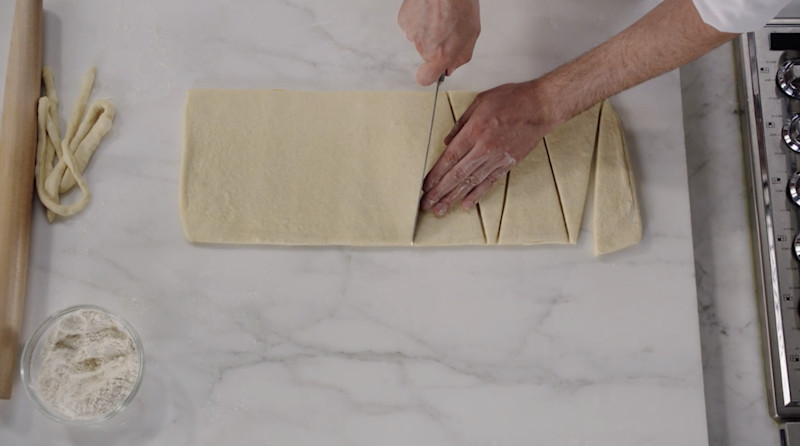 Dominique Ansel cutting croissant dough into triangles