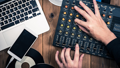 Person using audio mixer with laptop and iPhone on desk