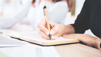 Woman writing in notebook with pen on desk