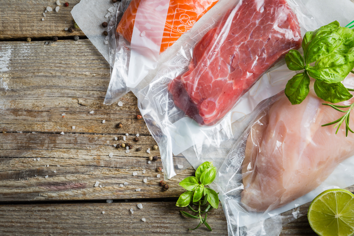 Meats and fish in plastic bag with herbs and lime on wood