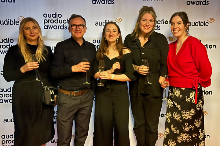 A group of five people are standing in front of a backdrop that says "Audio Production Awards" 