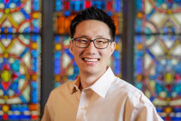 a man smiling with stained glass behind him