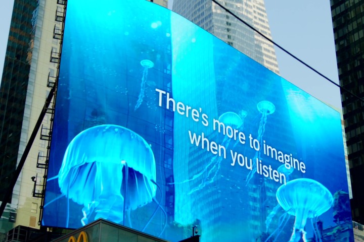 An augmented reality screen showing jellyfish moving through blue water, against a background of two skyscrapers. The screen also displays the words "There's more to imagine when you listen."