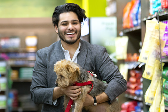 A man in a blazer carrying a small terrier with a red leash walks through a pet store in Newark.