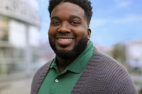 Audible employee My'Chal Wilkins is pictured outside of the Audible Headquarters in Newark, NJ wearing a green polo shirt and grey cardigan.