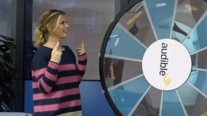 Emilia Fox stands next to the Audible dialect wheel of the tongue twister challenger crossing her fingers in hopes of a dialect she can do easily.