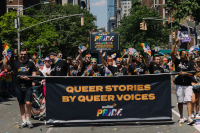 Members of the Audible community walk proudly in the 2022 New York City Pride Parade, holding a banner that says "Queer Stories by Queer Voices... Audible Pride" and holding rainbow-colored fans and flags.
