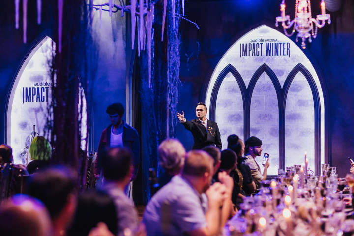 a person performing to a group of people in a gothic dinner hall
