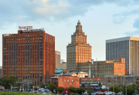 The Newark skyline appears at dusk as the light turns golden on the red brick buildings. The sky is blue with wisps of clouds. Two of Audible's office buildings appear in the foreground.