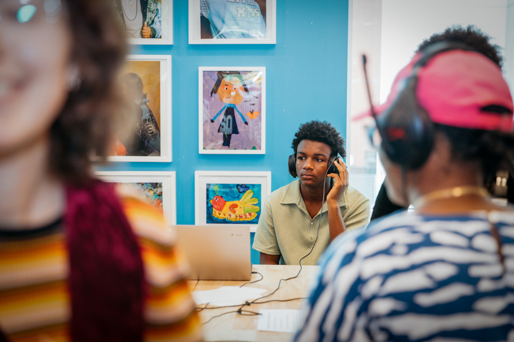 A teenager sitting at a desk, with a laptop in front of him. He's wearing headphones. 