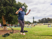 A man balances barefoot on a slack line strung between two trees in a park.