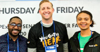 Three Audible employees stand in front of a while backdrop wearing Audible t-shirts.