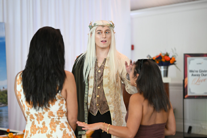 Two eventgoers speak to a man dressed as a high-fantasy elf. 