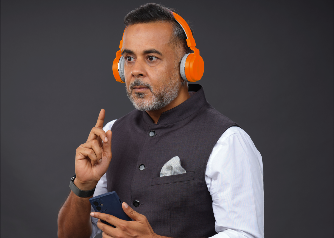 Chetan Bhagat holds a phone and wears orange headphones, listening to an audiobook.