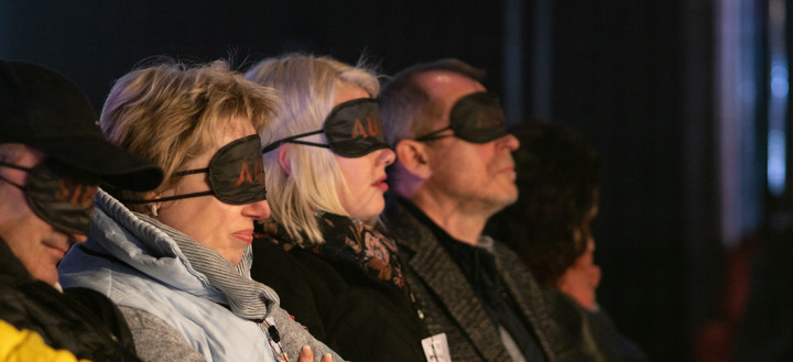 People sit in the audience with eye masks on listening to audio clips.