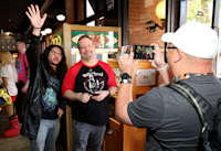 A photo of Jeff Hays and Matt Dinniman at Audible's arcade-themed activation, "The Safe Room," during San Diego Comic-Con. In the photo, Jeff and Matt are posing for a picture that's being taken by a fan.