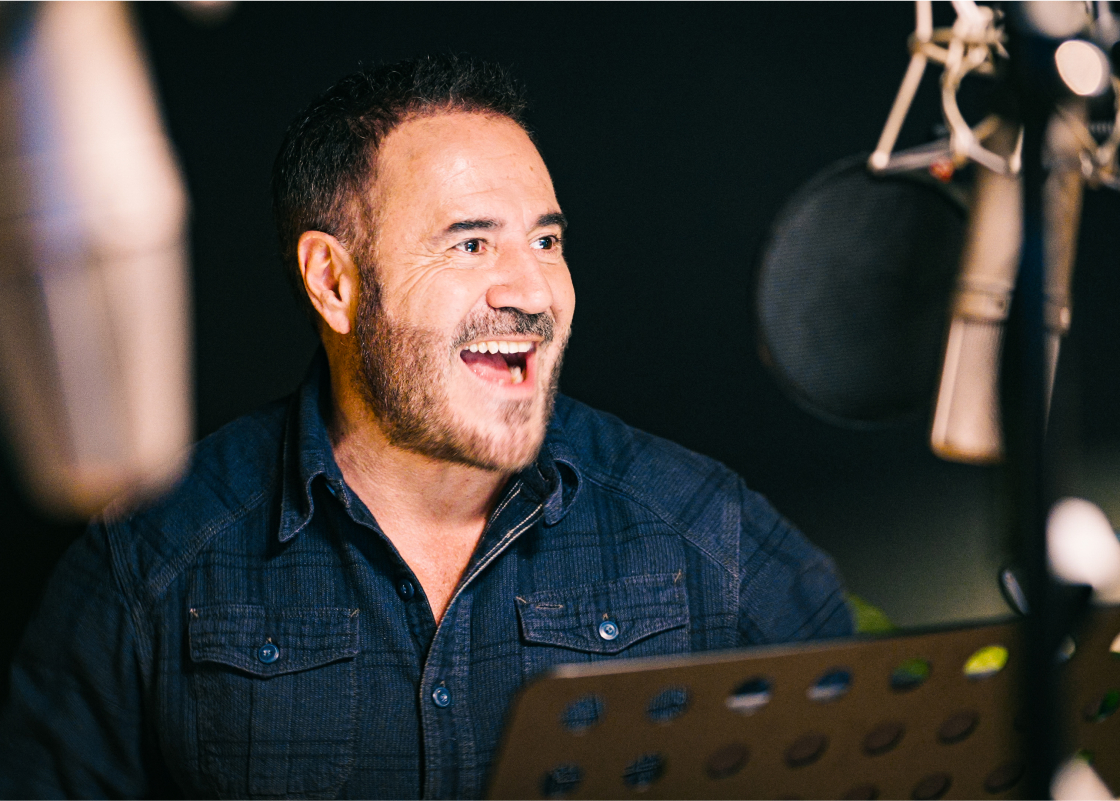 José Garcia stands in front of a microphone in a recording studio narrating an audiobook.