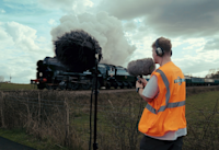 A person standing in a field records the sounds of a passing steam train. 