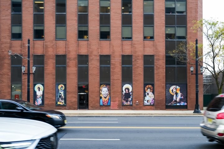 a building with a lot of windows with collages of women and cars driving by
