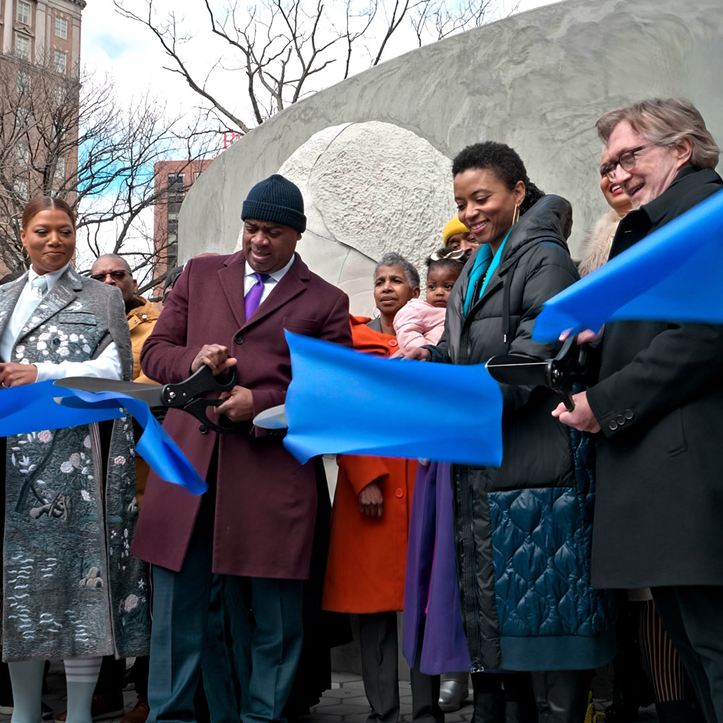 A few people stand in front of a monument cutting a large blue ribbon to mark its unveiling.