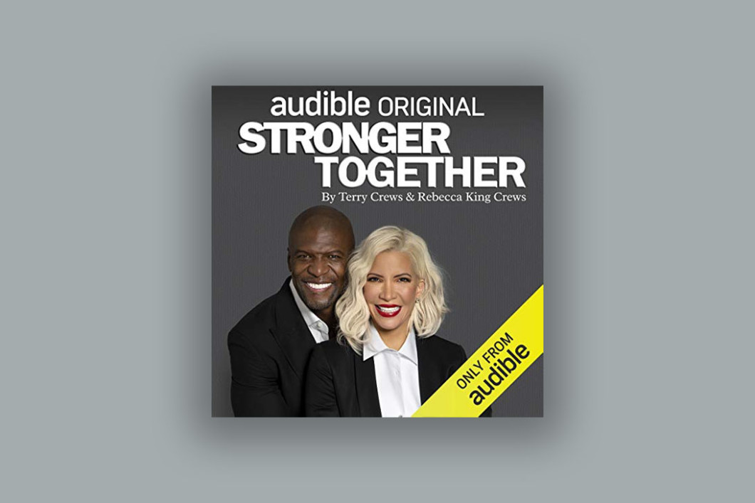 Set on a grey background, the cover art of "Stronger Together" showcases the authors Terry Crews and Rebecca King-Crews both in a black suit jackets and white shirts. The title "Stronger Together" is in large white text above their heads. 