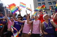 People crowded together to watch the NYC Pride March. They're wearing pink and purple #BeEpic shirts and waving rainbow-colored Pride flags.