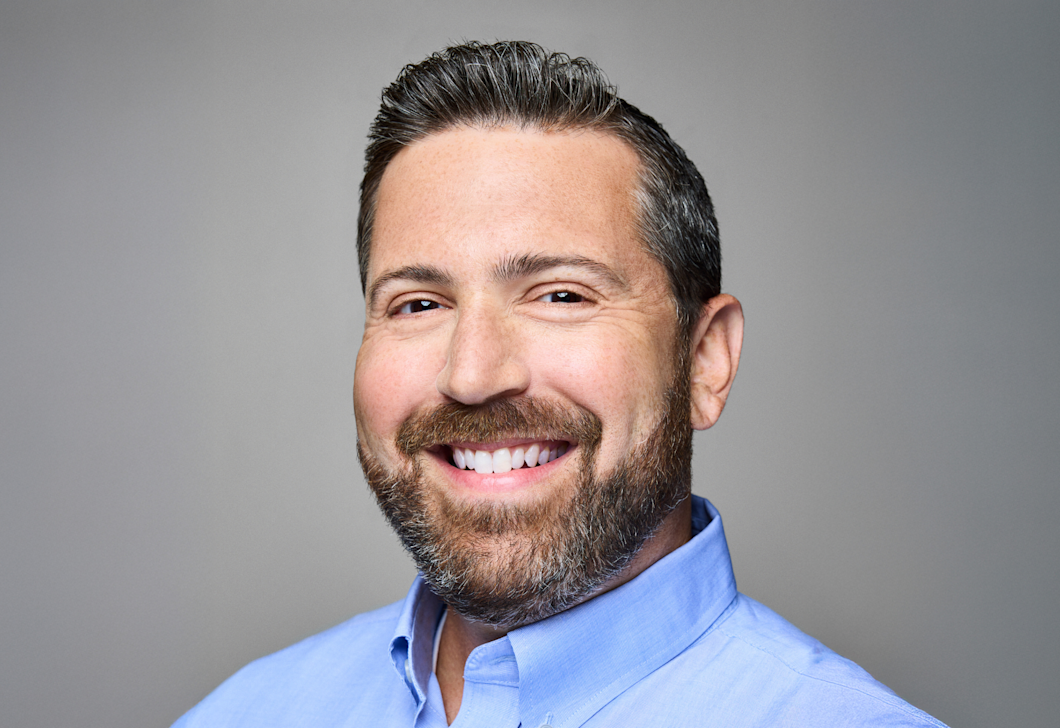 A headshot of Lee Jarit, who's smiling. Lee has a beard and is wearing a blue button-down shirt. 