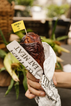A person's hand holding a turkey leg wrapped in a wrapper that says "Eat Me" and with a flag on it saying "Smoky AF"