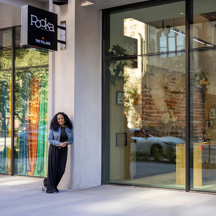 A woman stands outside the glass windows of a store with the sign with the store name "Pooka" above her head.