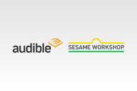 The Audible logo and the Sesame Street logo sit side-by-side against a light grey background. The Audible logo is the name in black type with an orange chevron at the end of the "e". The Sesame Workshop logo has the name in grey type with a yellow line with a bell curve in the middle over the top and a straight green line underneath.  