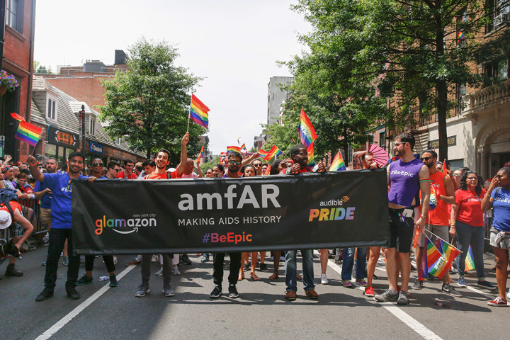 People marching in the NYC Pride March carrying a large amfAR banner.
