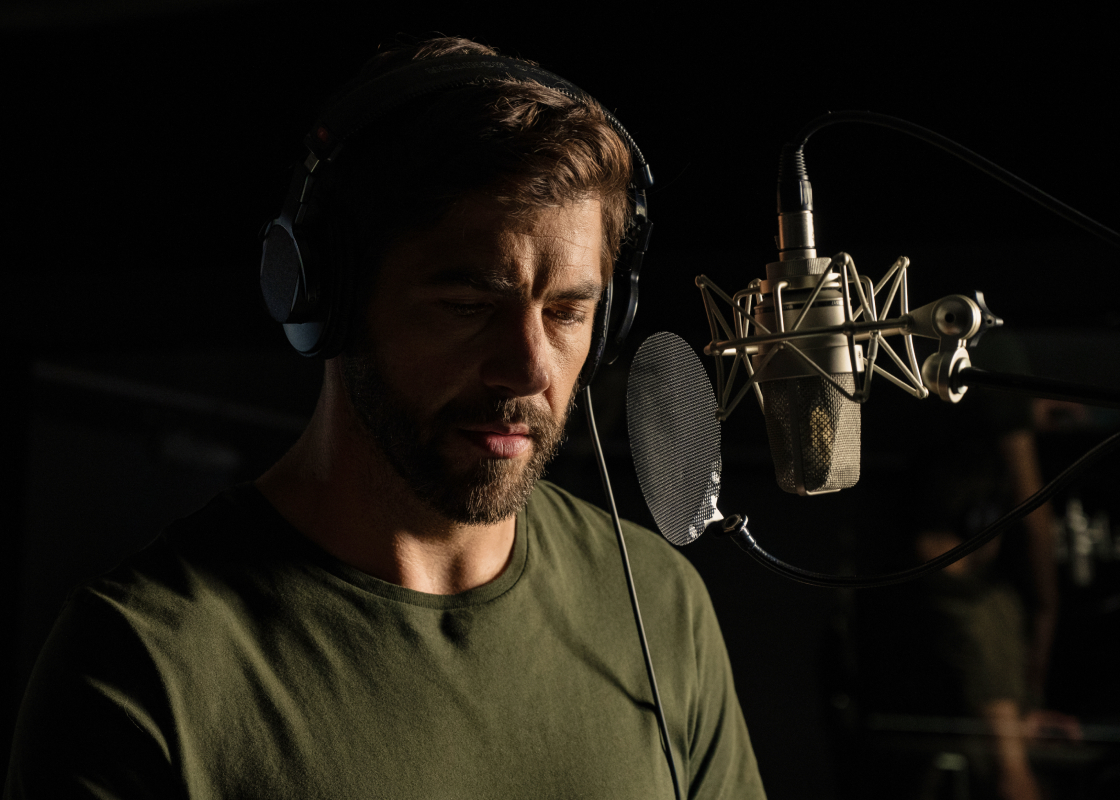 Pierre Yves Cardinal stands at a microphone in a recording studio narrating an audiobook. 