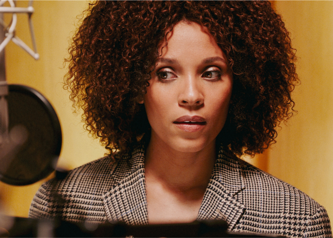 Stéfi Celma stands at a microphone in a recording studio narrating an audiobook.