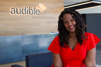 A woman in a red dress sitting in front of the Audible logo.