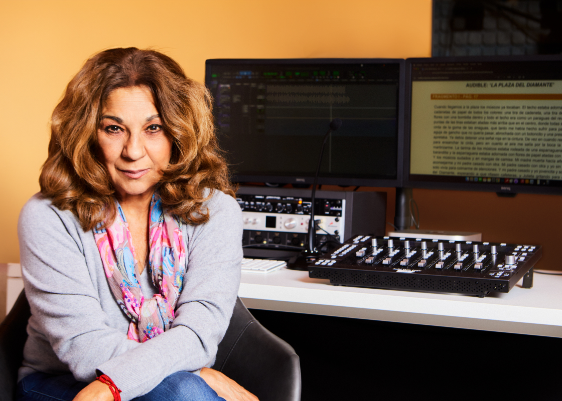 Lolita Flores sits in a recording studio facing the camera, a mixing board and monitor sit on a table behind her.