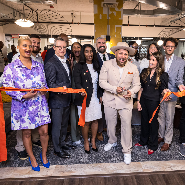 A crowd of people stand at a ribbon cutting ceremony, the guy at the center having just cut it to mark the space's opening.