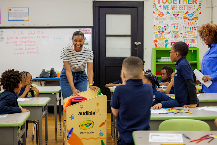 A teacher rolls an Audible + Crayola story cart through a classroom to the delight and excitement of the young students.