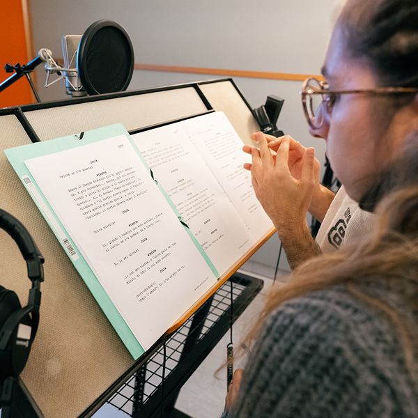 A printed script sits on a stand, a mic behind it and an actor before it, her face in profile.