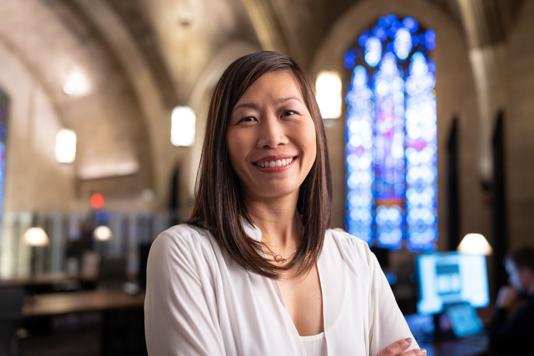 Audible’s CFO and Growth Officer Cynthia Chu is sitting in Audible's Innovation Cathedral. She is wearing a white sweater and looking at the camera smiling. Behind her you can see stained glass windows. 