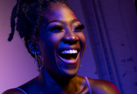 Amber Iman smiles and is glowing with a purple hue coming from a spotlight.
