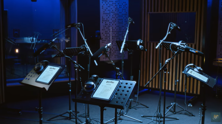 Several microphone stands and tablet devices with Harry Potter and Audible logos in a dark recording studio with blue lighting.