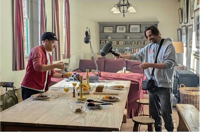 A photo of two sound designers capturing audio of dinner plates and silverware moving around a table. 