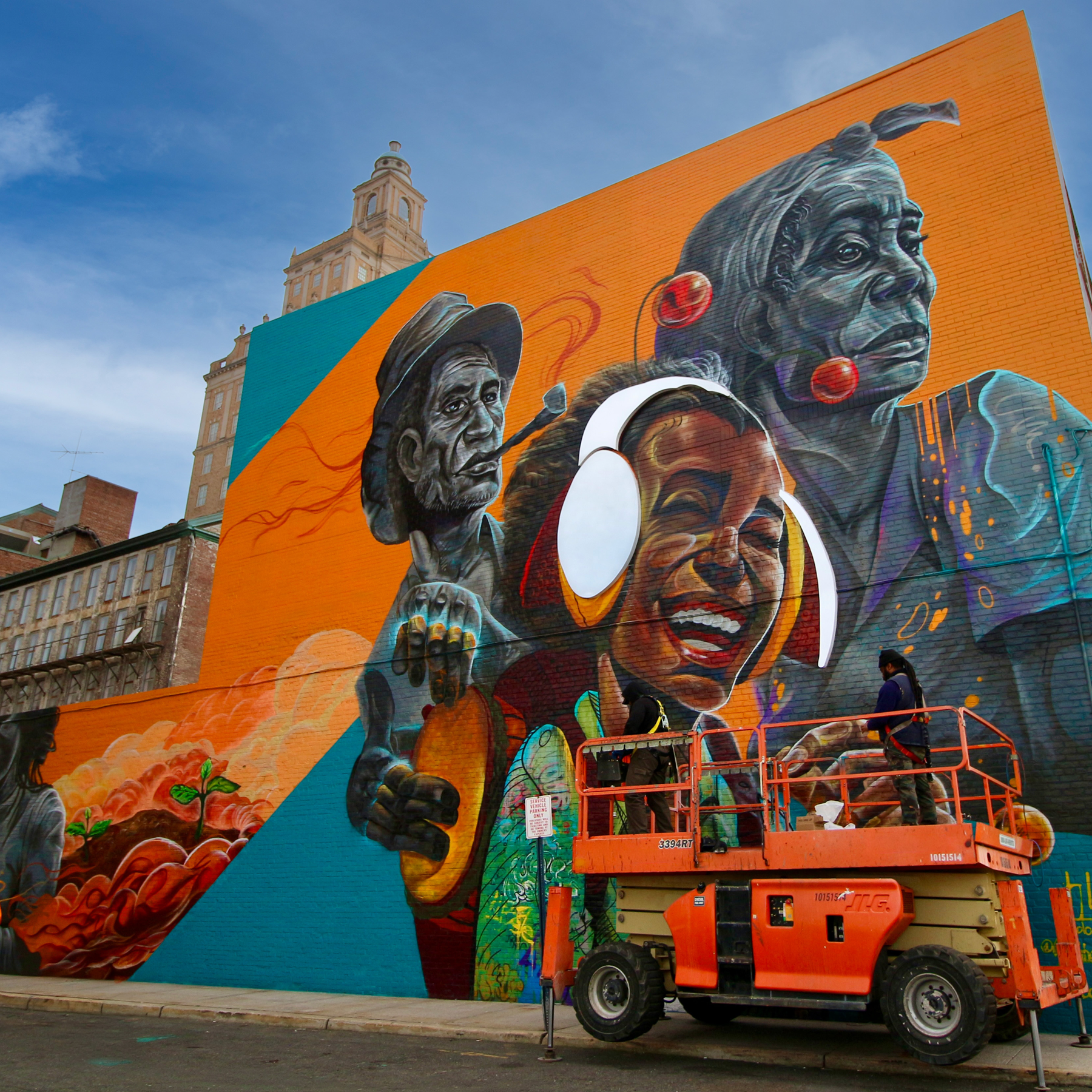 An artist jumps with joy in front of her mural of a man listening with headphones on.